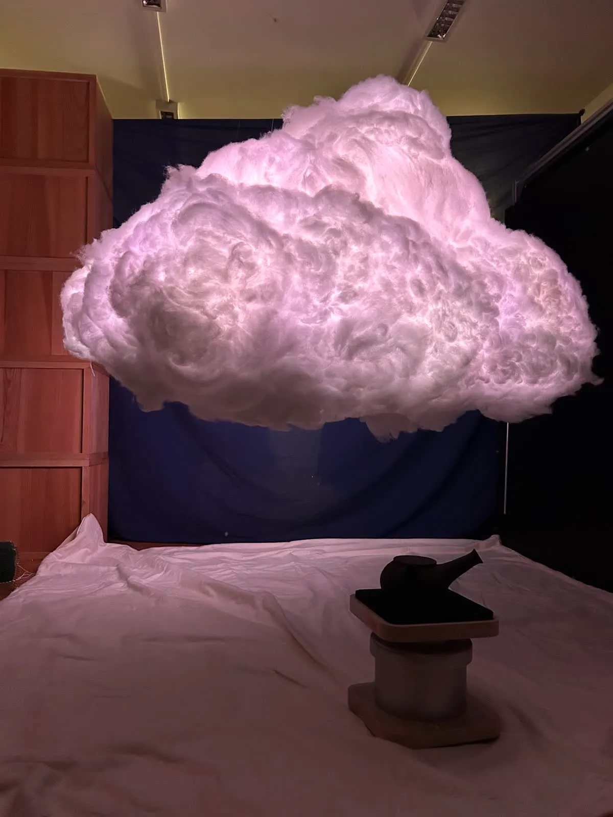 The cloud glowing pale pink above white sheets, with a teapot on a small pedestal below
