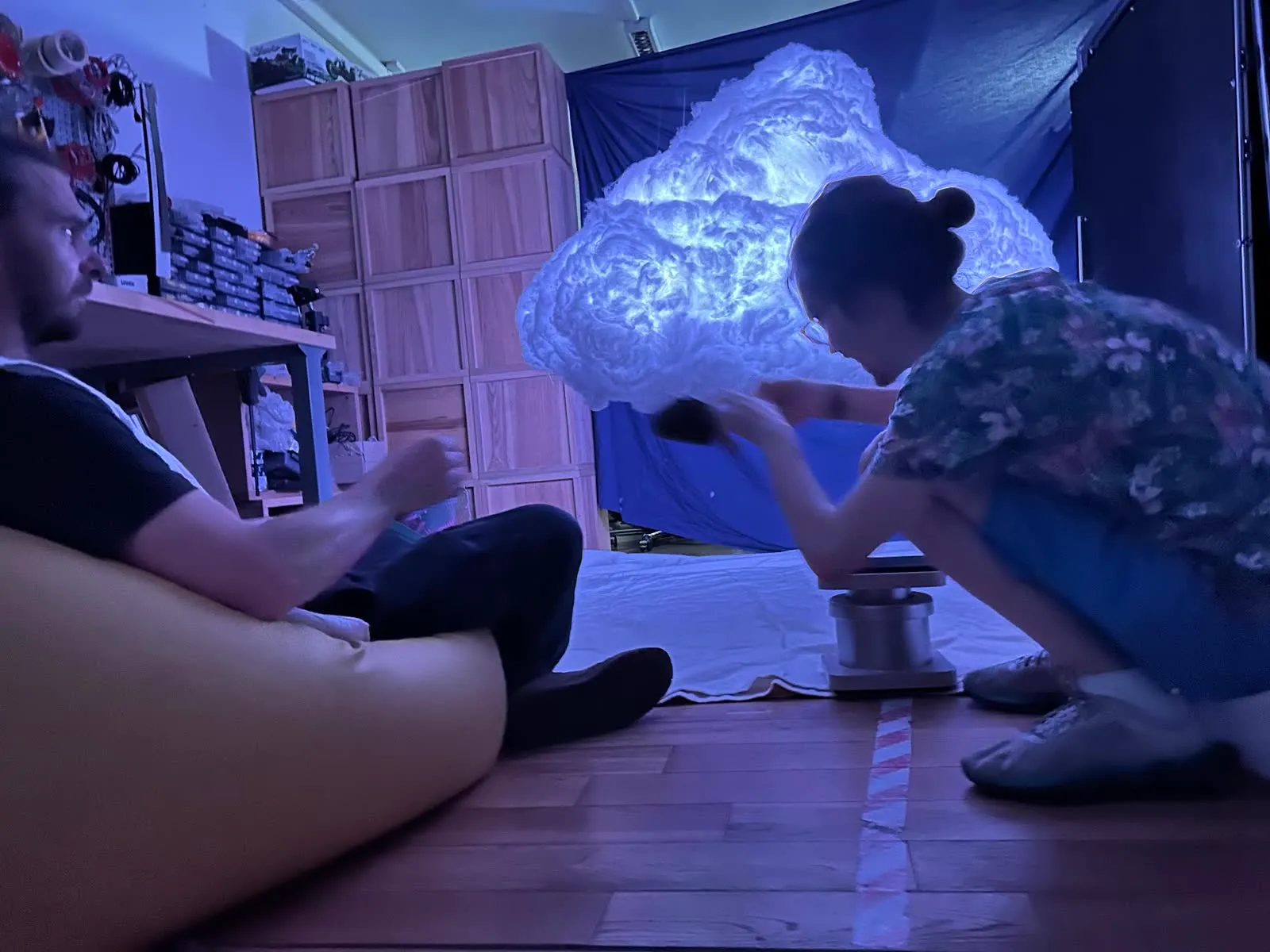 Pouring tea beneath the cloud, lit blue, while someone watches from a beanbag