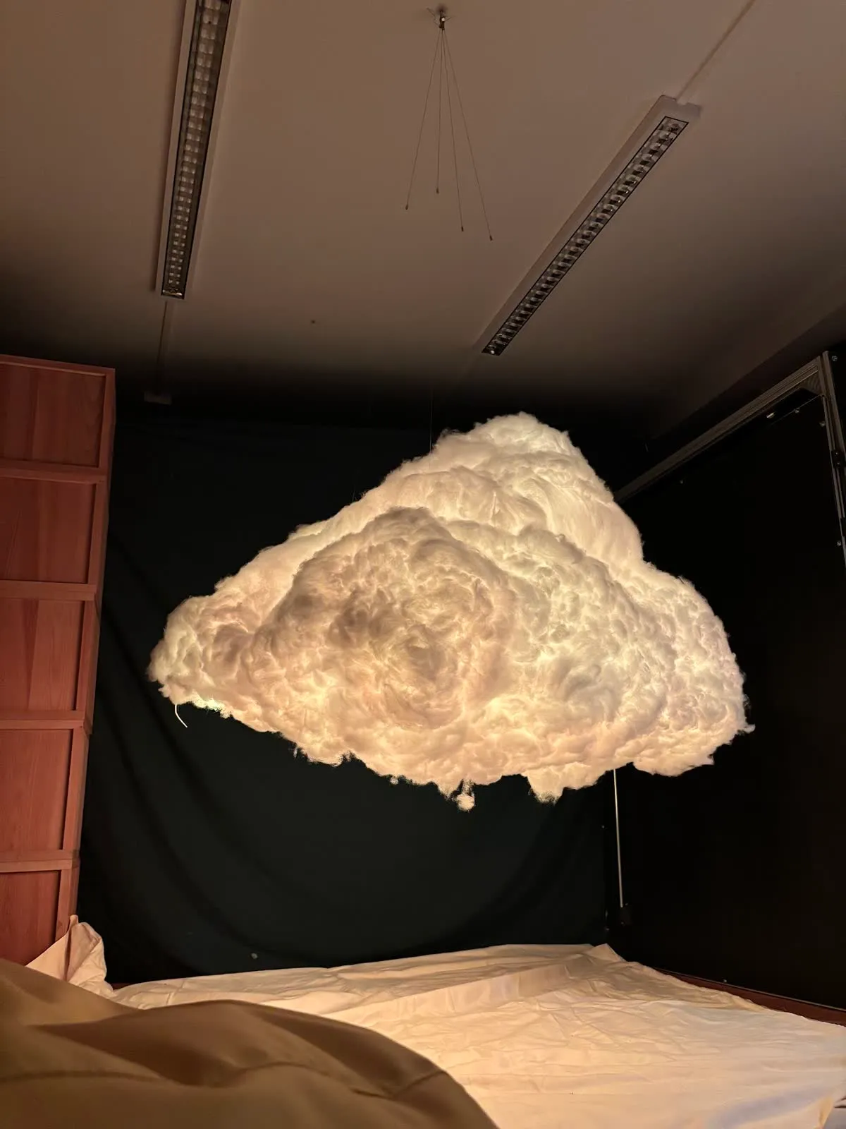 Looking up from the floor at the fibre cloud glowing warm white, hanging from the ceiling in a dark room.