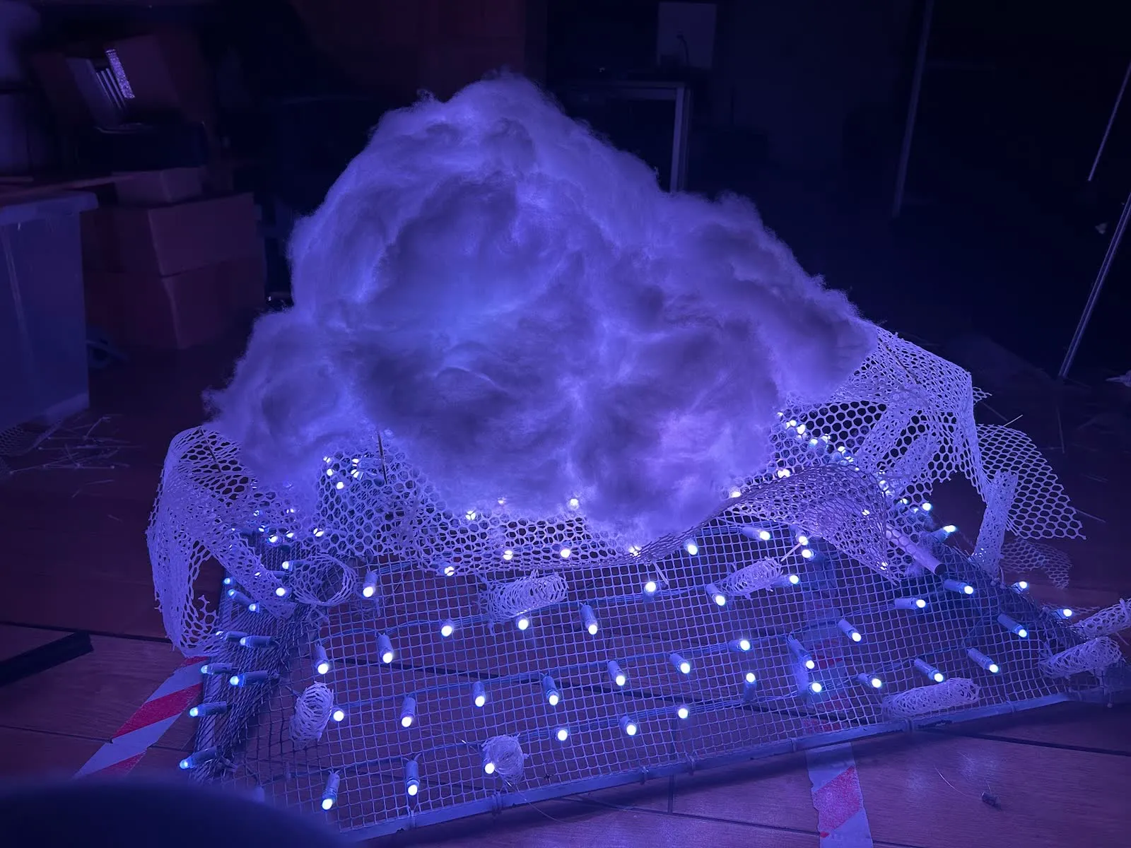 A mound of white fibre glowing violet on top of a mesh frame strung with LED pixels