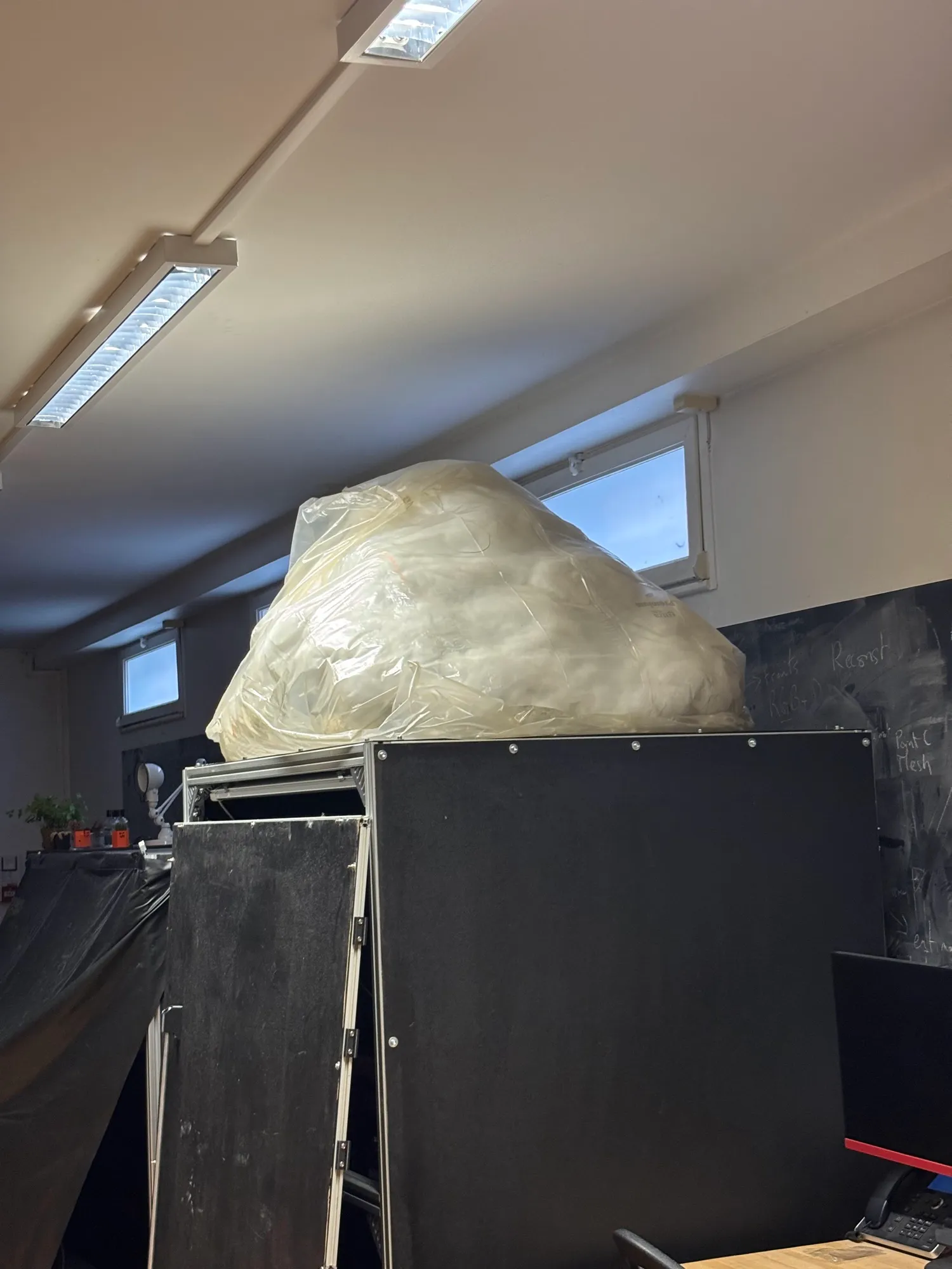 The pilot cloud packed into a large clear bag, sitting on top of a black cabinet in the workshop.