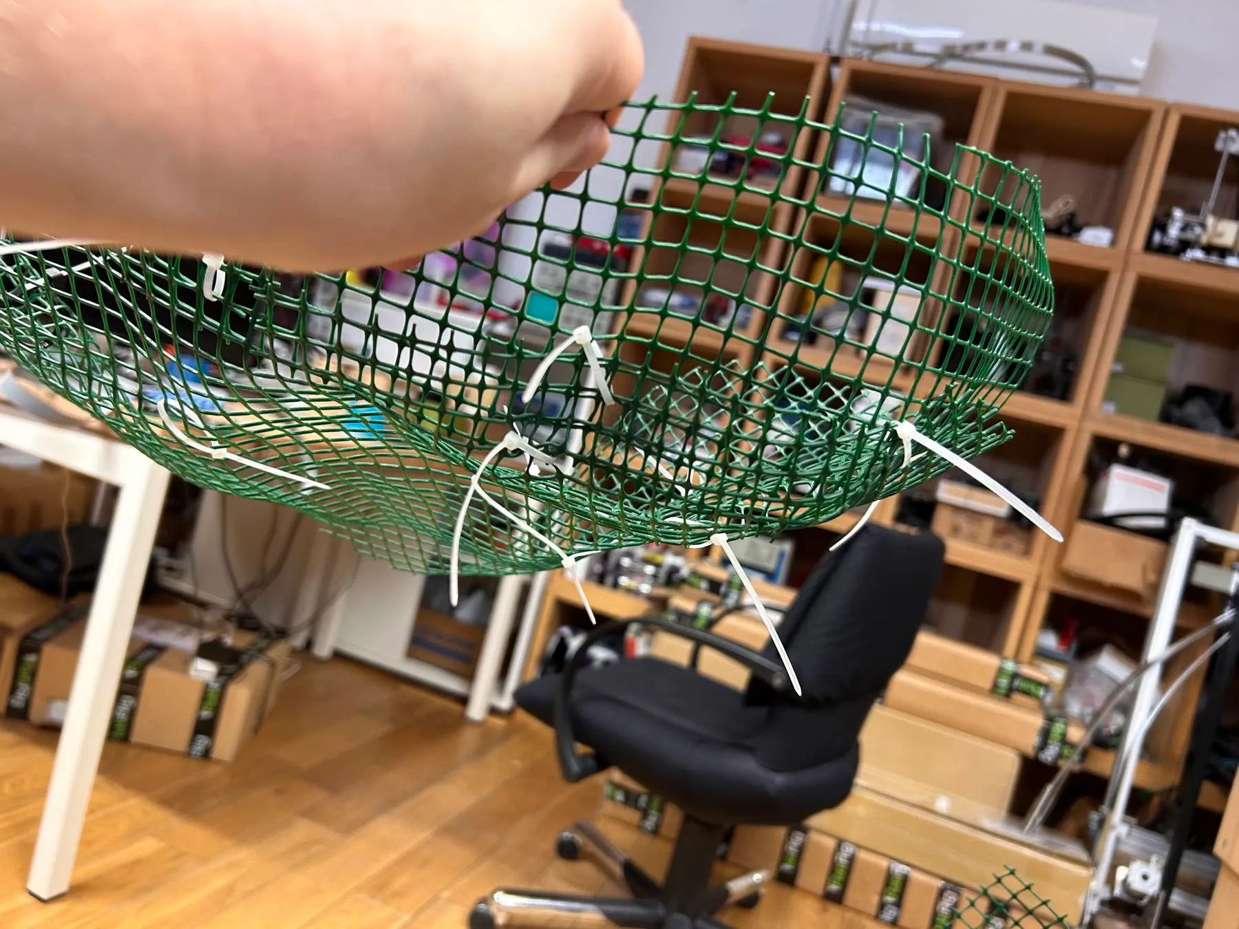 A hand holding up a first attempt at a cloud made of green plastic mesh