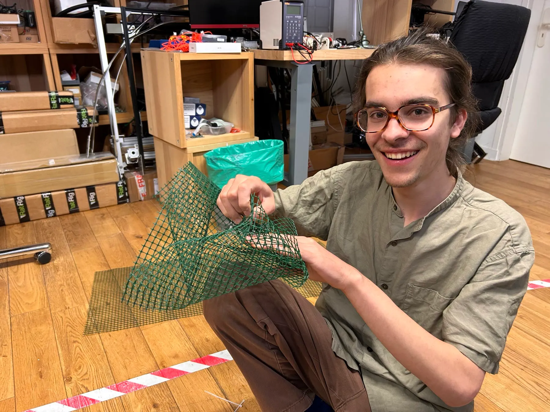 Zéphir kneeling on the studio floor, shaping a sheet of green plastic mesh into a cloud form.