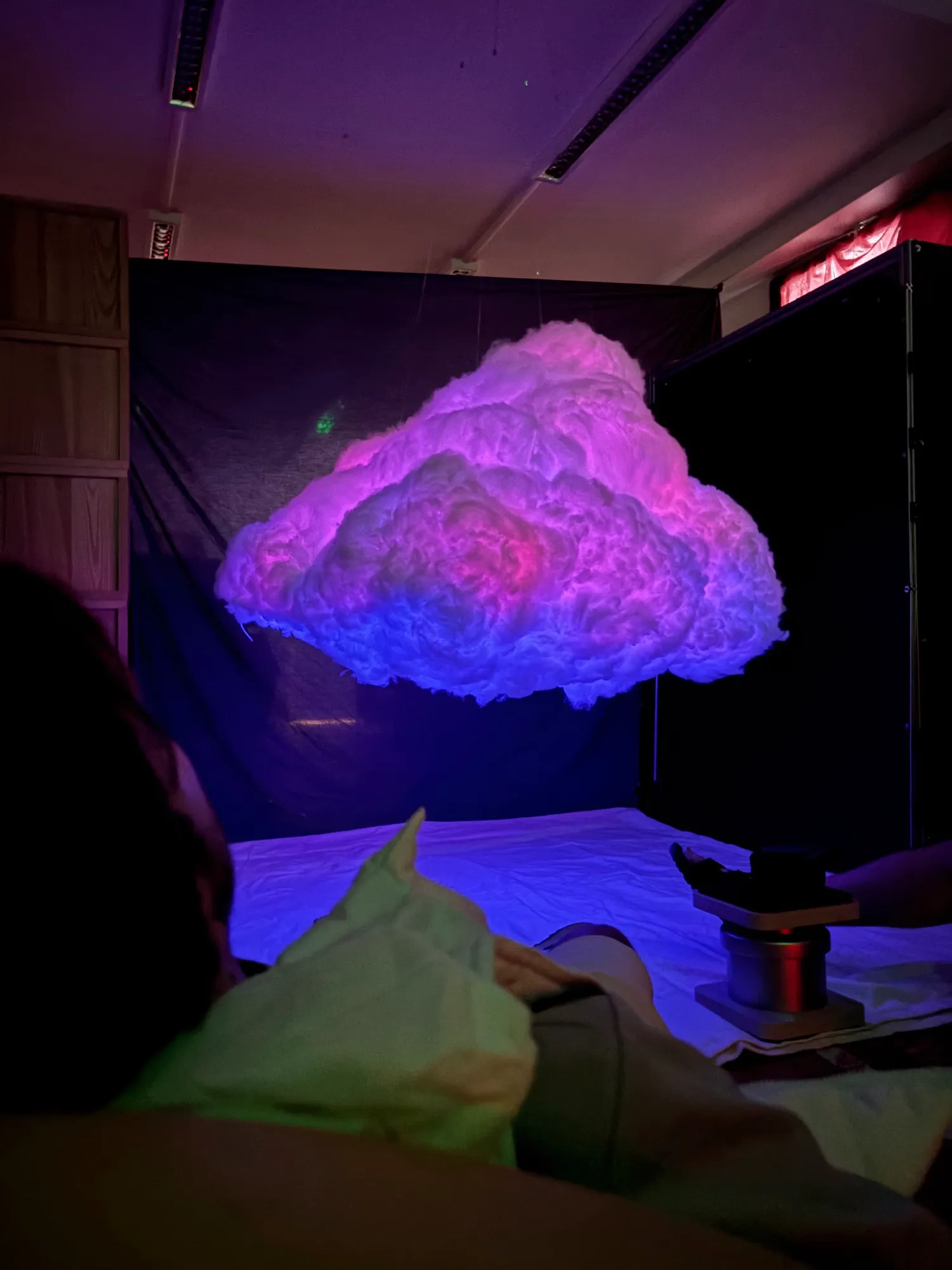The cloud glowing pink, purple and blue above the sheets, seen from the floor.