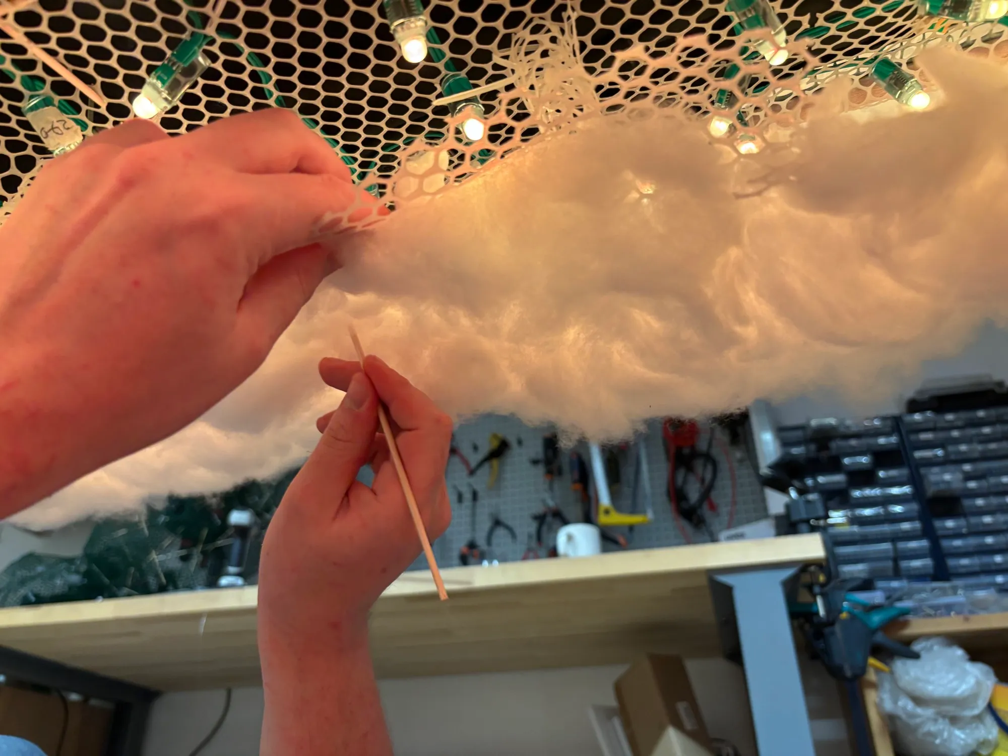 Close-up from below: hands pushing fibre into the hexagonal mesh with a bamboo skewer.