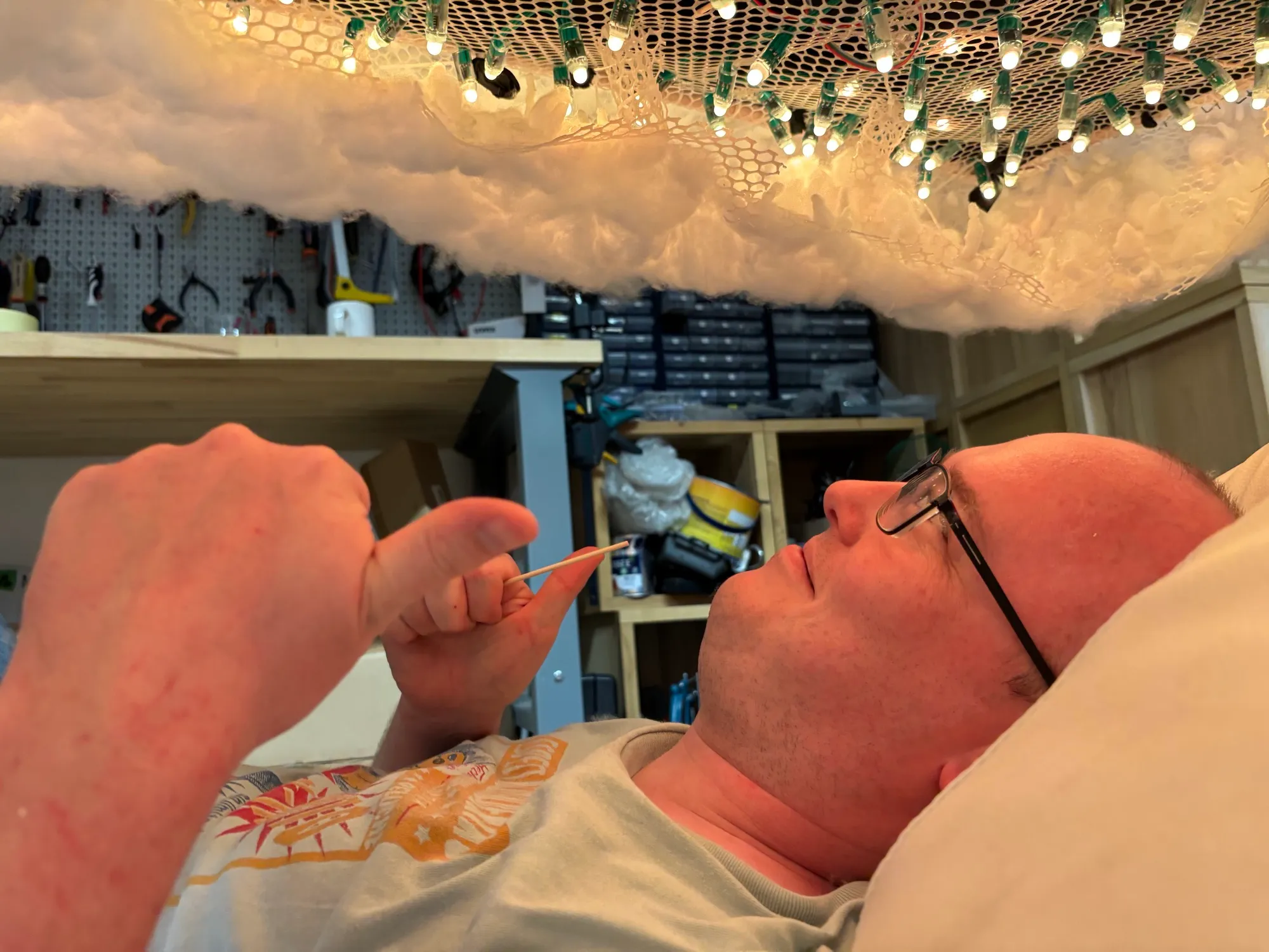 Lying under the lit cloud, giving a thumbs up.