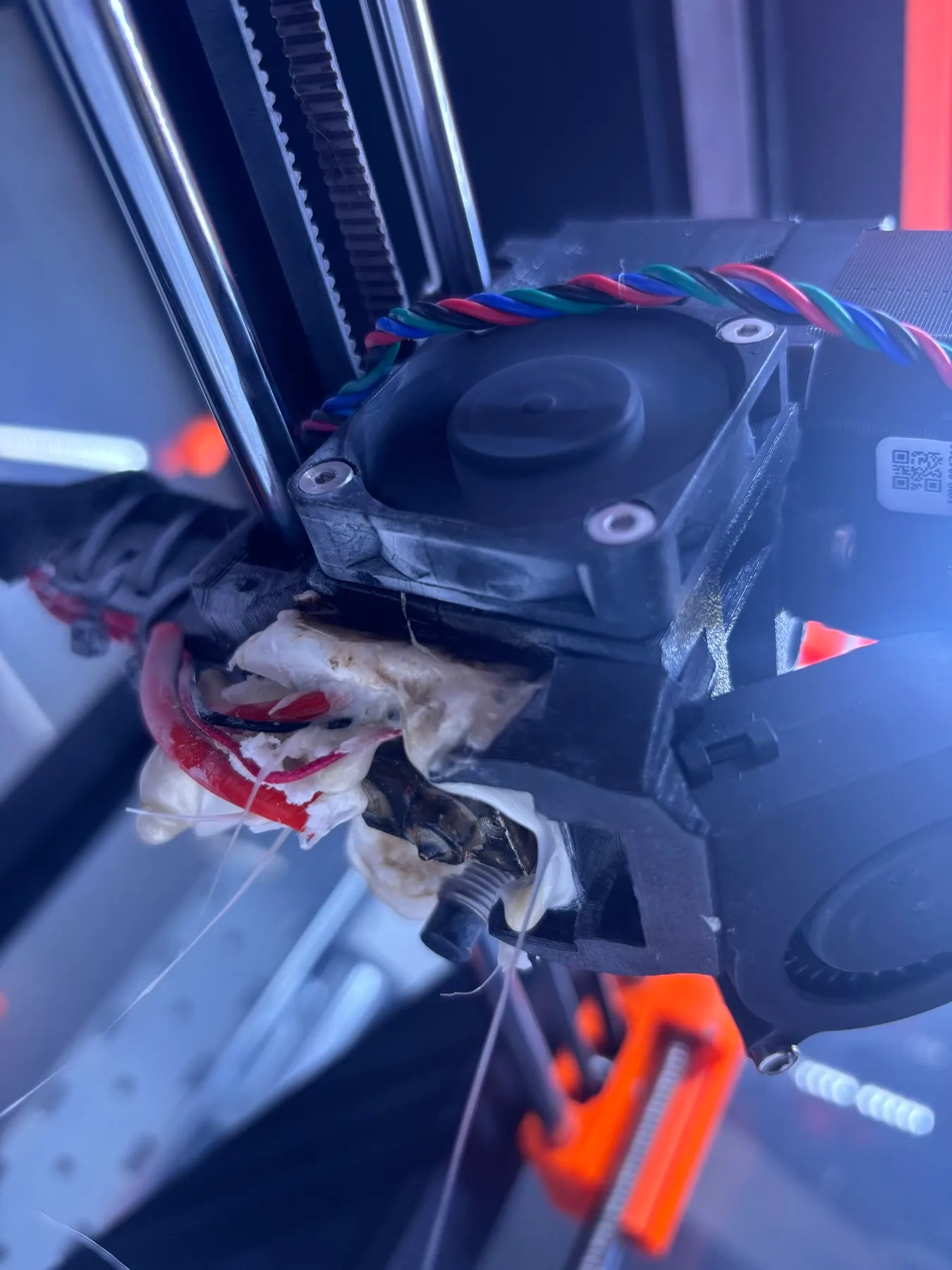 The printer’s hot end from below, buried in melted white filament with its red heater wires trapped inside