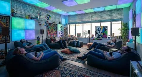A brightly lit version of the room crowded with colourful posters, toys and glowing ceiling tiles.