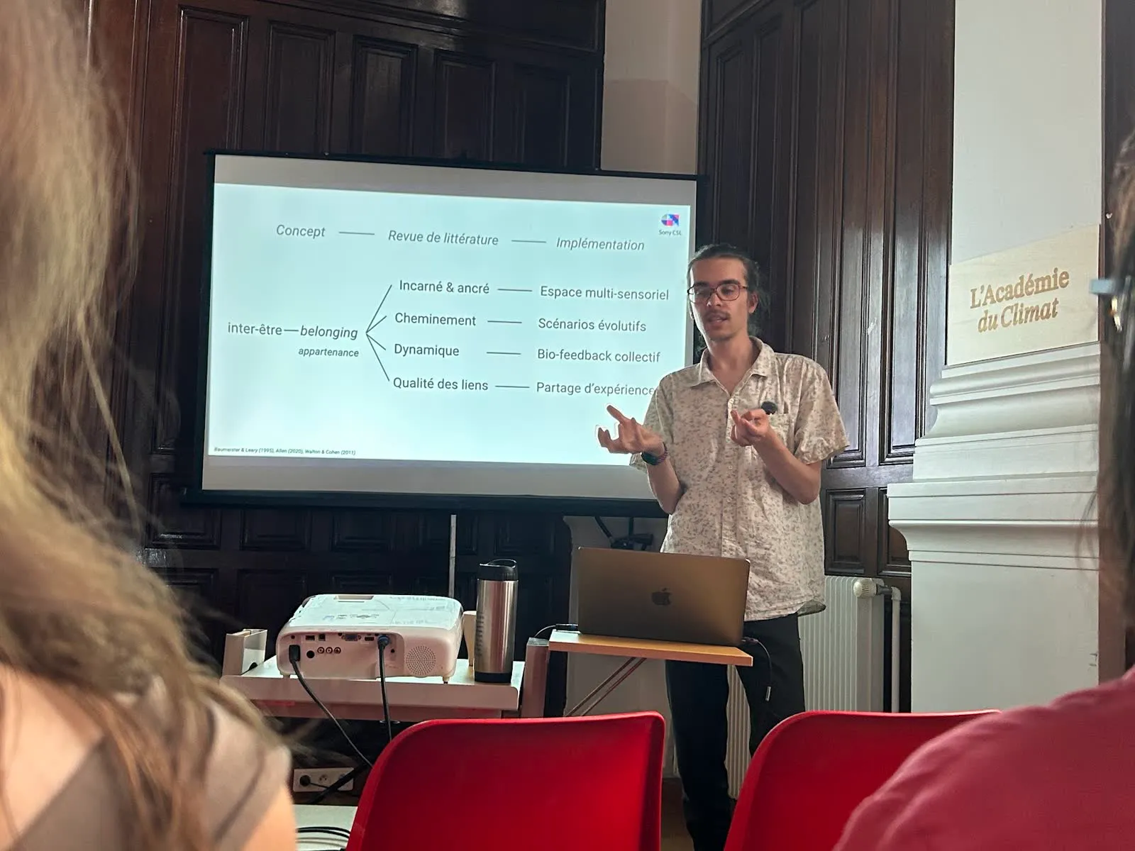 Zéphir presenting in a wood-panelled room at the Académie du Climat, beside a slide mapping belonging to design choices.