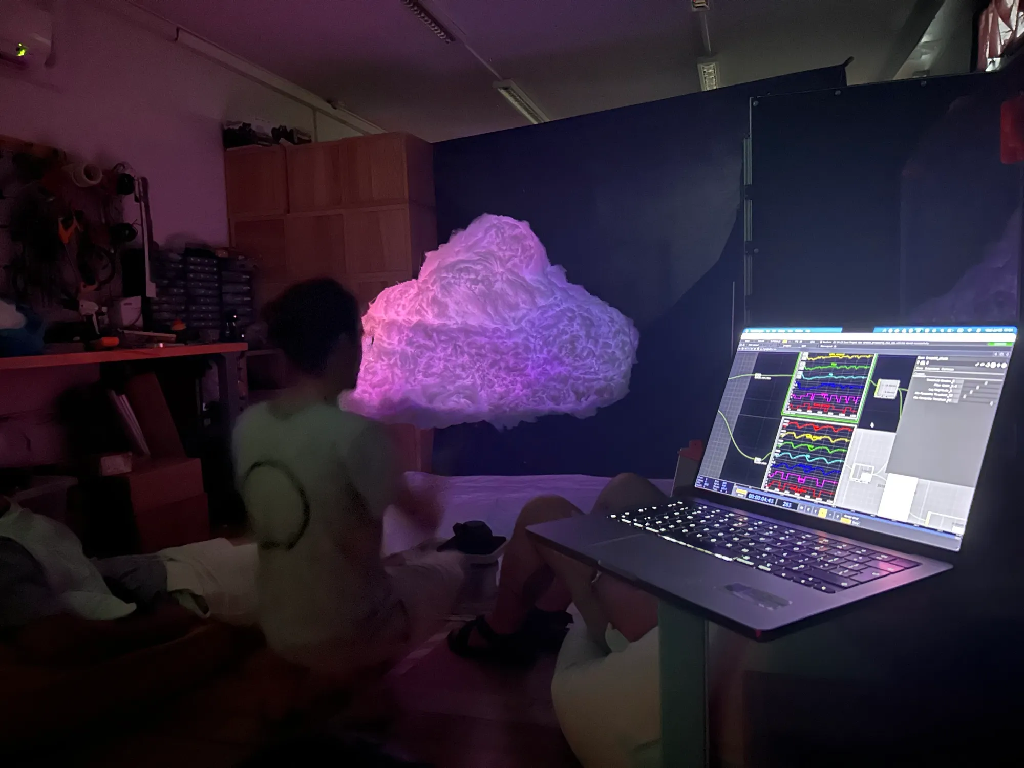 A laptop running TouchDesigner with breath waveforms from the belts, the cloud glowing behind it.