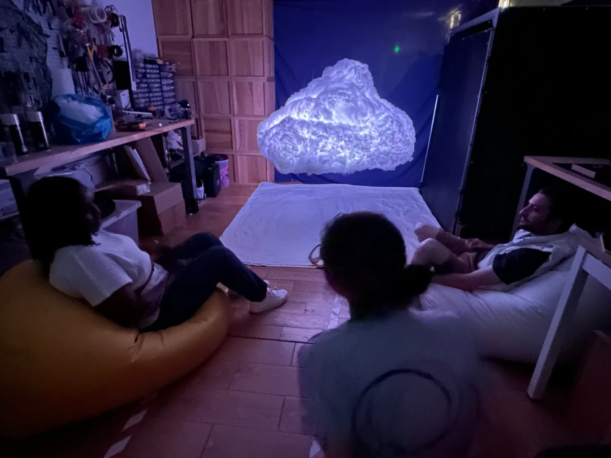 Visitors lounging on beanbags and sheets beneath the glowing cloud in front of a blue backdrop.