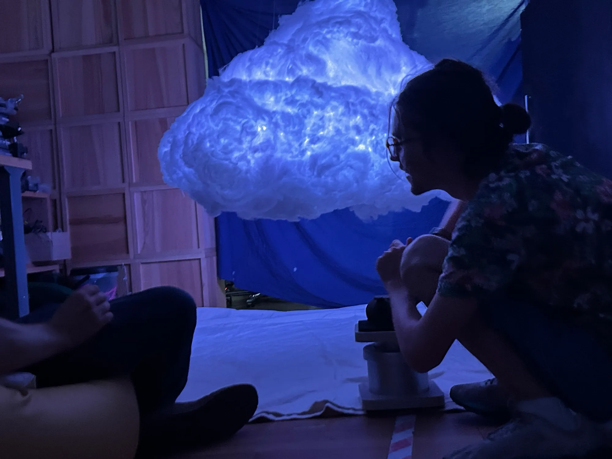 Zéphir pouring tea beneath the cloud, lit blue.
